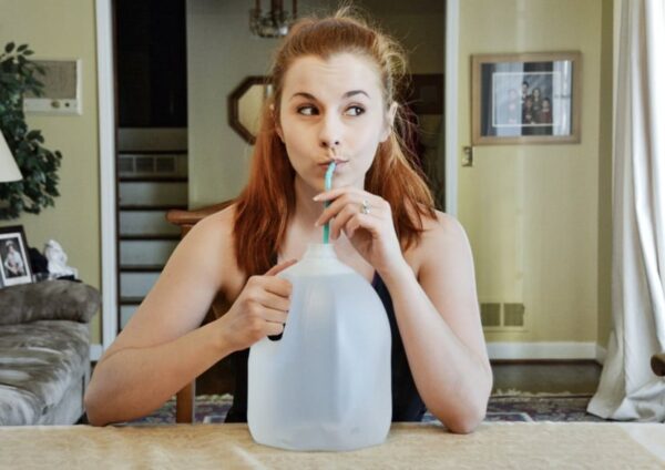 Red headed woman Reese Woods sips on a straw that's inserted into a gallon jog of water