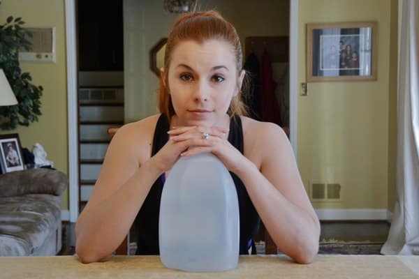 Red headed woman Reese Woods folds hands on top folds hands on top of gallon jug of water while resting her chin on her hands and smiling