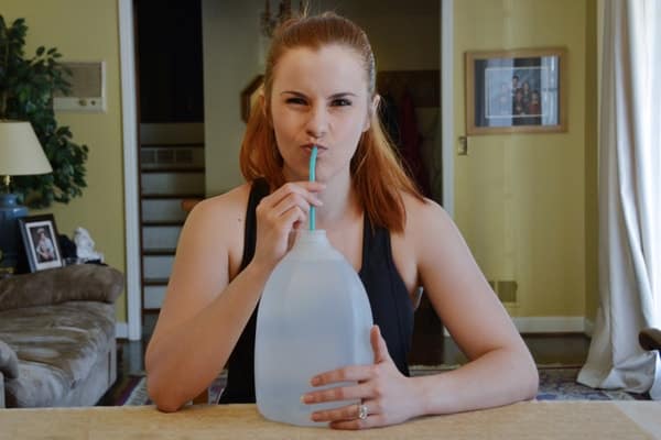 Red headed woman Reese Woods makes a silly, playful expression while taking a sip from a straw in a gallon jog of water
